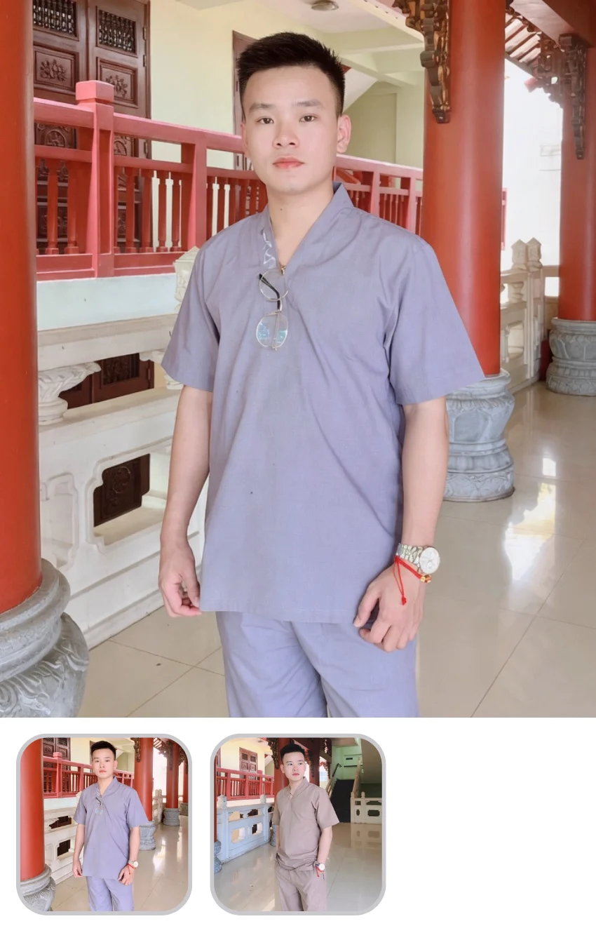 Young man in a light gray traditional outfit posing inside a temple with red pillars; sunglasses hang from his shirt.