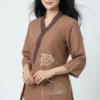 Asian woman wearing a brown embroidered tunic and matching pants, standing against a light background with a gentle smile.