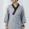 Young woman wearing a gray traditional Chinese top with a dark brown collar and purple floral embroidery, posing against a neutral backdrop, hands at sides.