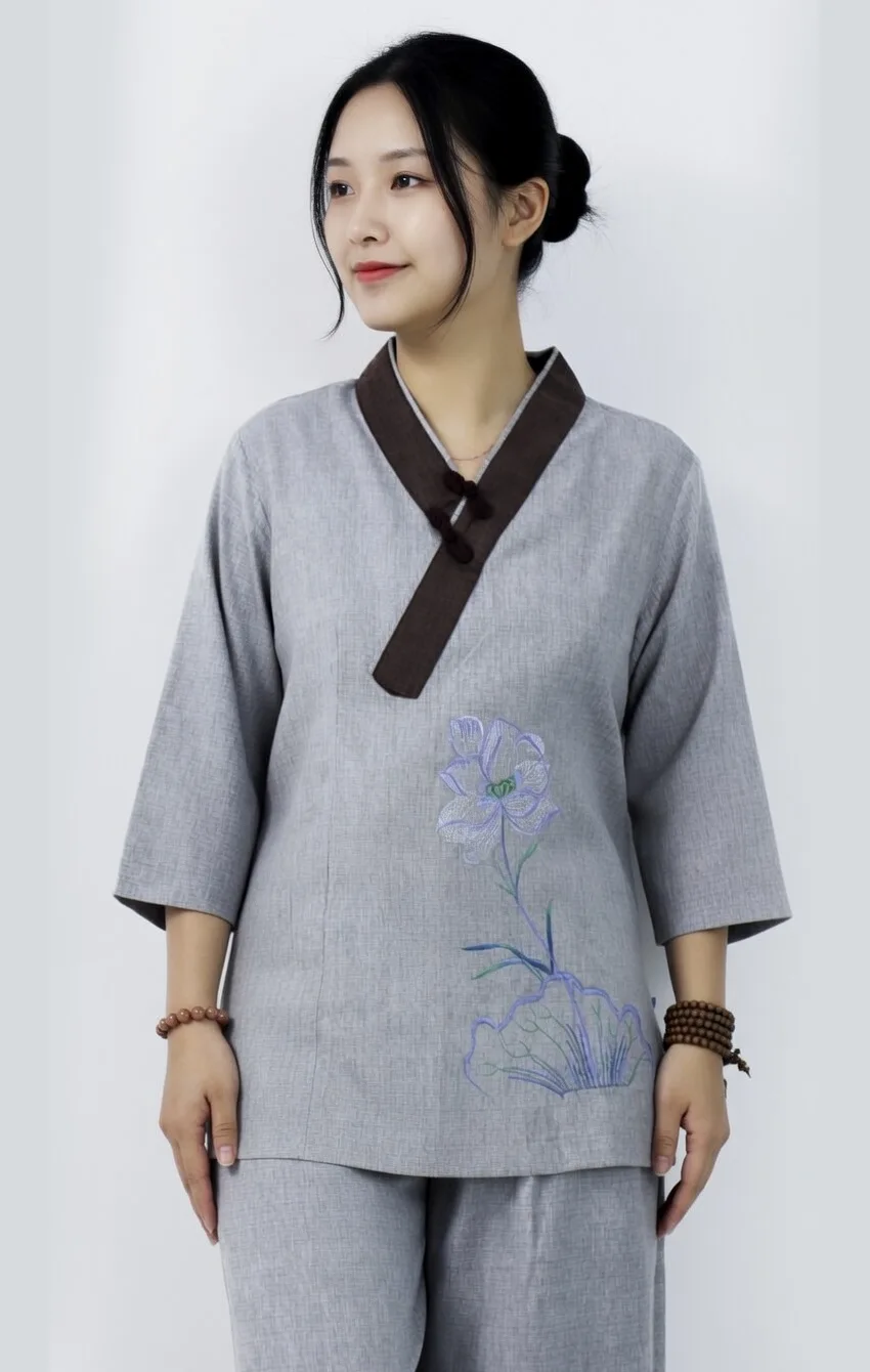 Young woman wearing a gray traditional Chinese top with a dark brown collar and purple floral embroidery, posing against a neutral backdrop, hands at sides.