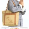 Pháp Phục Woman in a gray traditional outfit carries a beige tote bag with brown straps and a lotus embroidery design