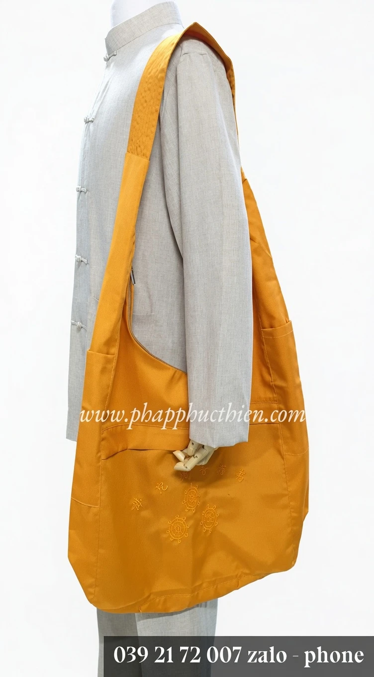Pháp Phục Orange large shoulder bag slung over a light gray traditional jacket on a mannequin with decorative embroidery on the bag near the bottom edge