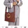 Man wearing a gray traditional Chinese outfit with a brown crossbody bag featuring a circular emblem on the flap, held by the strap across the chest.