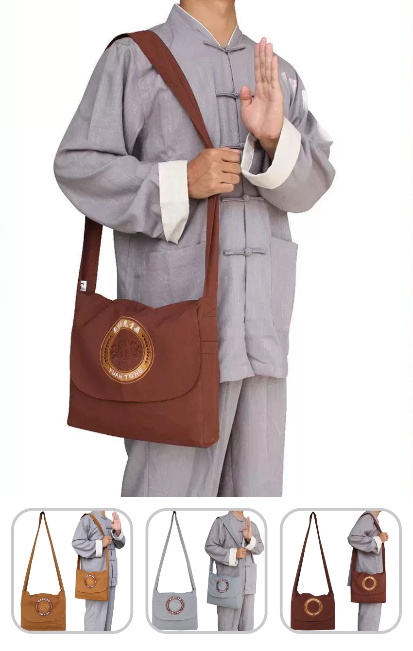 Man wearing a gray traditional Chinese outfit with a brown crossbody bag featuring a circular emblem on the flap, held by the strap across the chest.