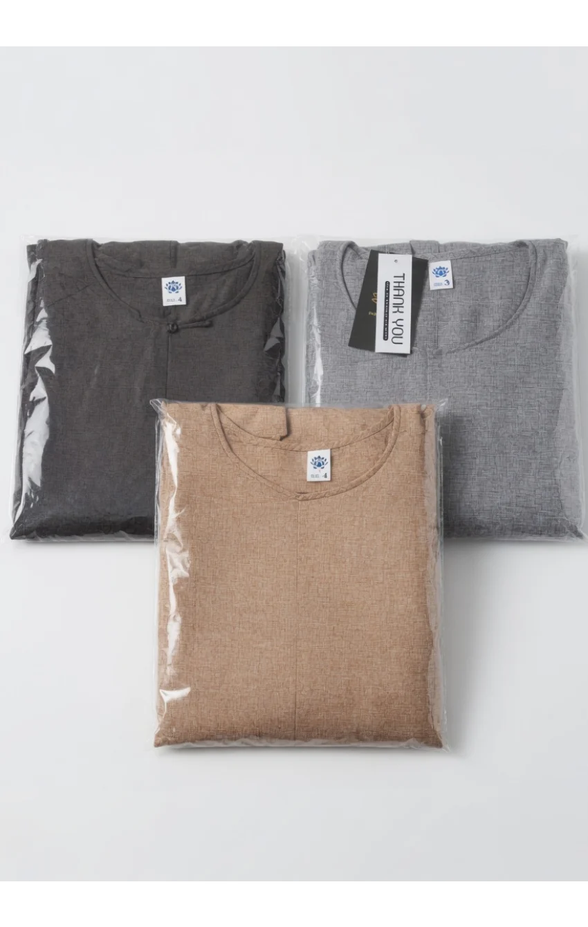 Three folded shirts in plastic packaging on a white surface, in black, gray, and tan colors with tags attached.