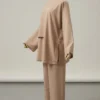 Beige loose-fitting two-piece suit on a dress form, featuring a long-sleeve tunic with side pockets and wide-leg pants.