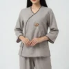 Woman wearing a light gray traditional tunic with brown trim and a stitched flower embroidery on the front.