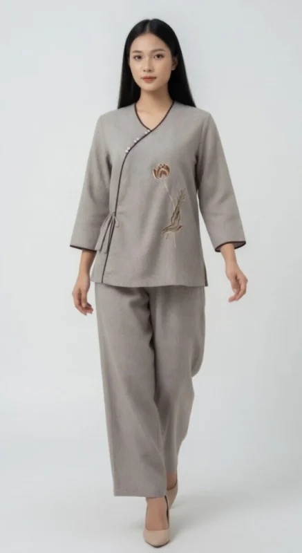 Pháp Phục Woman wearing a light gray wrap style tunic with floral embroidery and matching wide leg pants neutral toned outfit for a calm elegant look