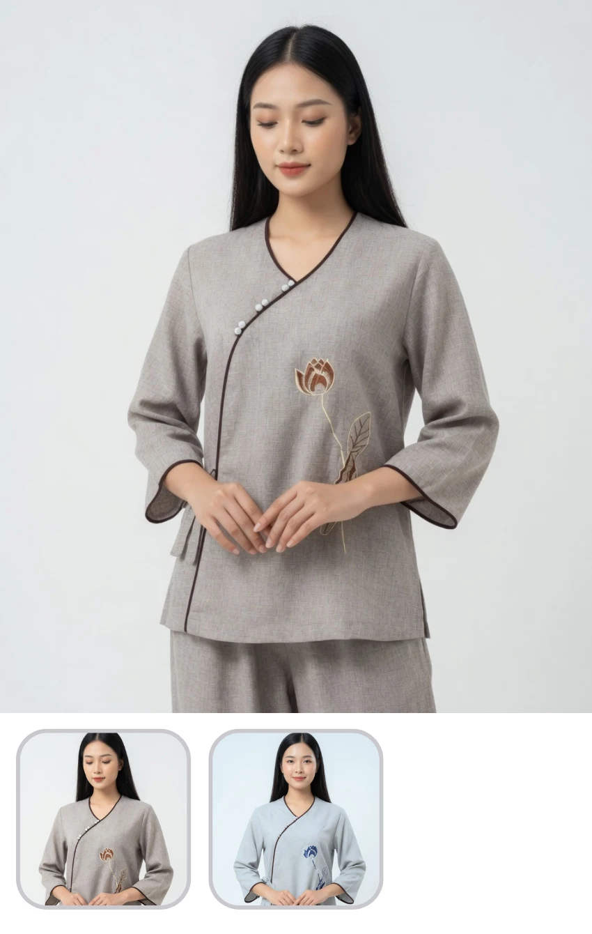 Woman in light gray wrap-style top with brown trim and lotus embroidery, posing with hands clasped.