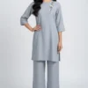 Woman modeling a light gray tunic with matching wide-leg pants and floral embroidery on the shoulder, beige heels.