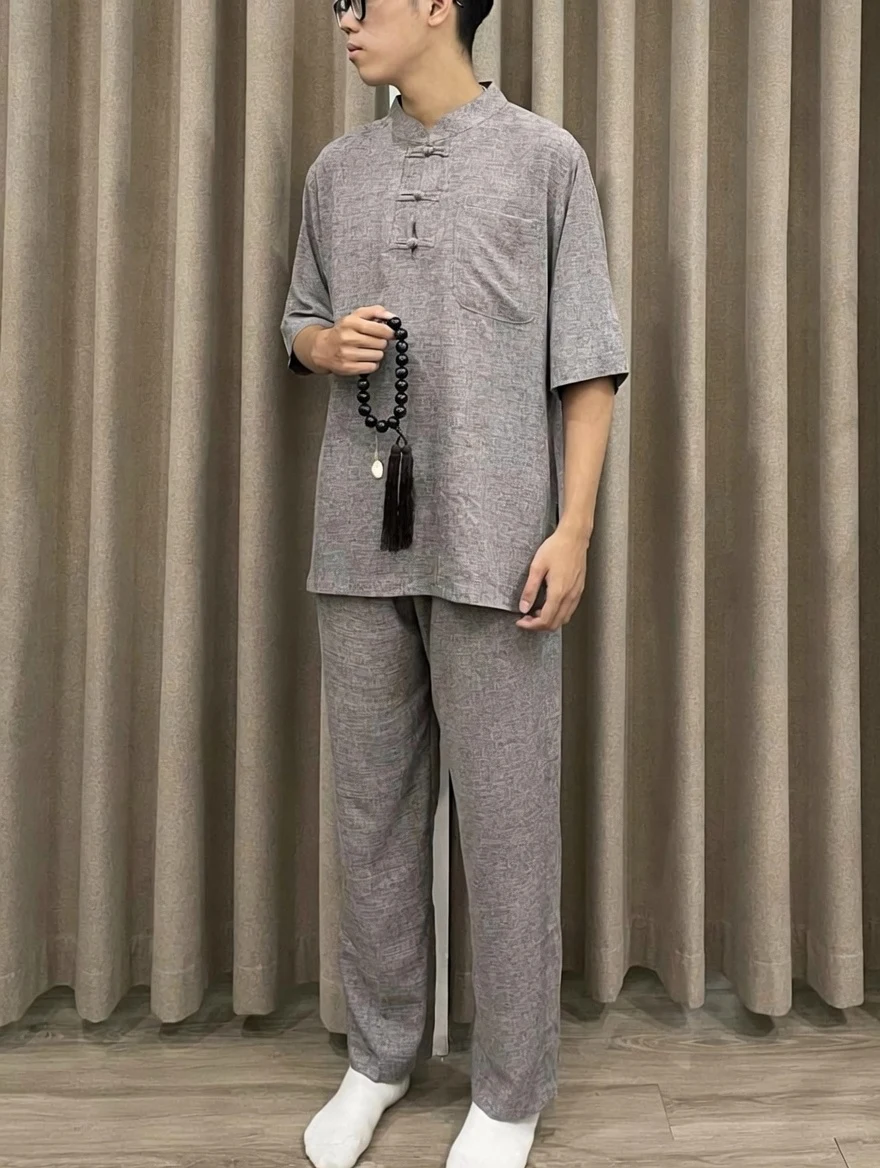 Pháp Phục Man wearing a gray traditional Chinese style tunic and pants holding a black bead mala with tassel against a curtain backdrop