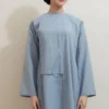 Woman in a light blue traditional tunic and matching pants, hair in a neat low bun with a decorative hairpin, standing against a plain wall.
