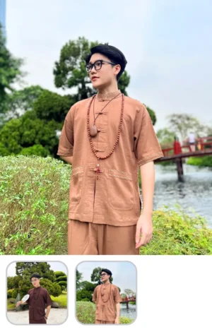 Man in brown traditional attire with glasses and beaded necklace standing by a pond with a red bridge in the background.