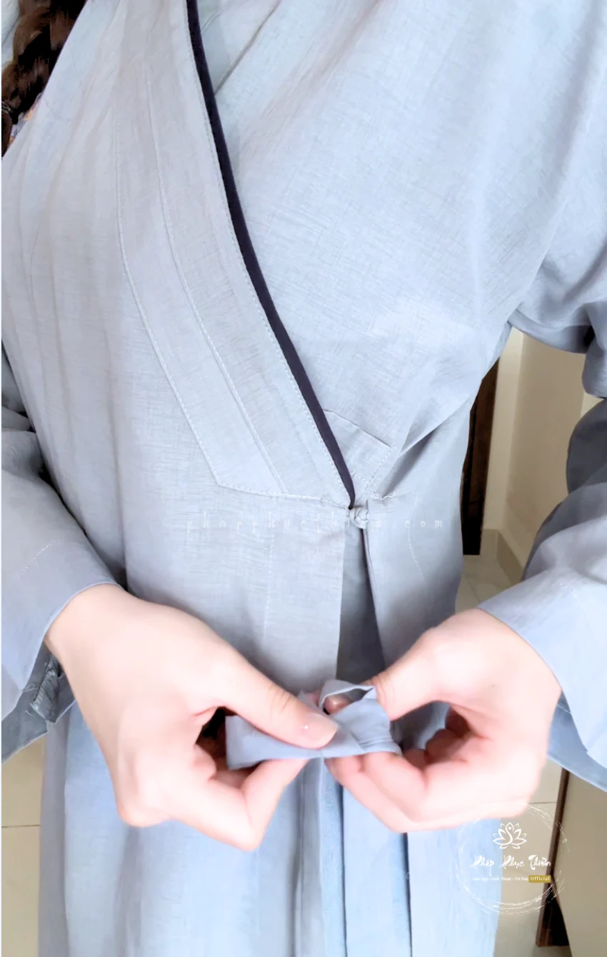 Pháp Phục Person in a pale blue robe tying a fabric belt at the waist close up
