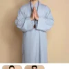 Pháp Phục Young man in light blue traditional robes stands against a beige backdrop hands pressed together in prayer wearing a bead necklace