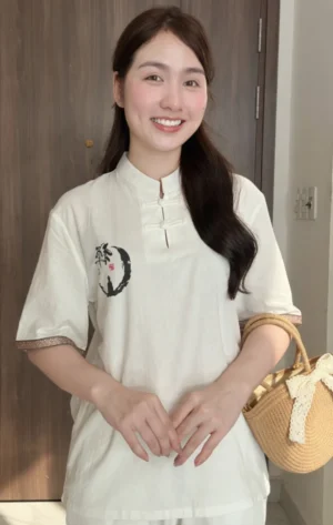 Pháp Phục Smiling woman indoors wearing a white top with Chinese knot closures holding a woven straw bag