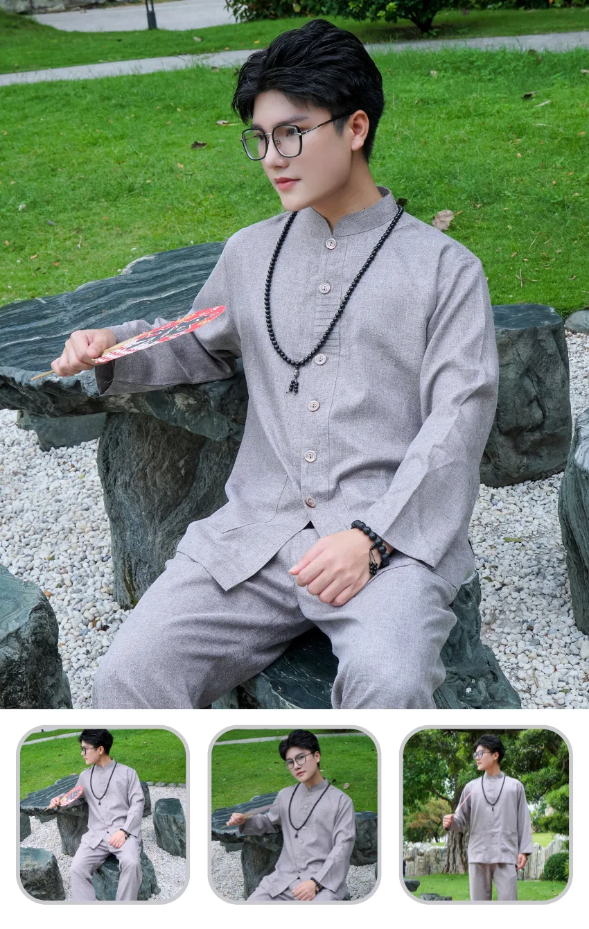 Young man in a gray traditional outfit with round glasses sits on rocks in a park, holding a red fan.