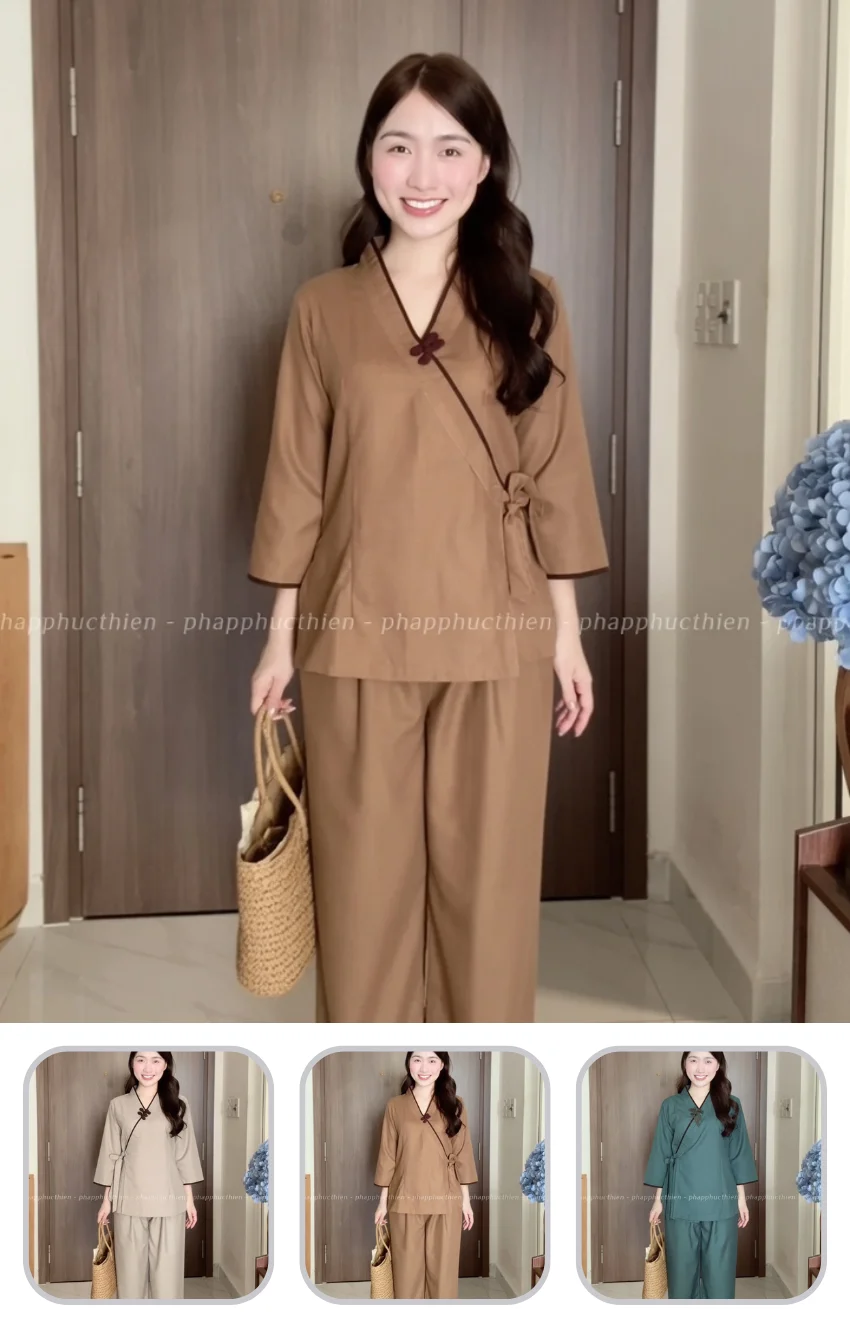 phap-phuc-nu-dep Woman in a camel-colored wrap tunic and wide-leg pants, holding a woven straw bag, standing in a doorway.