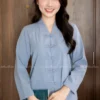 Smiling woman wearing a light blue mandarin-style top with frog buttons, indoors against wooden doors, holding a green booklet.