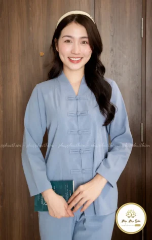 Pháp Phục Smiling woman wearing a light blue mandarin style top with frog buttons indoors against wooden doors holding a green booklet