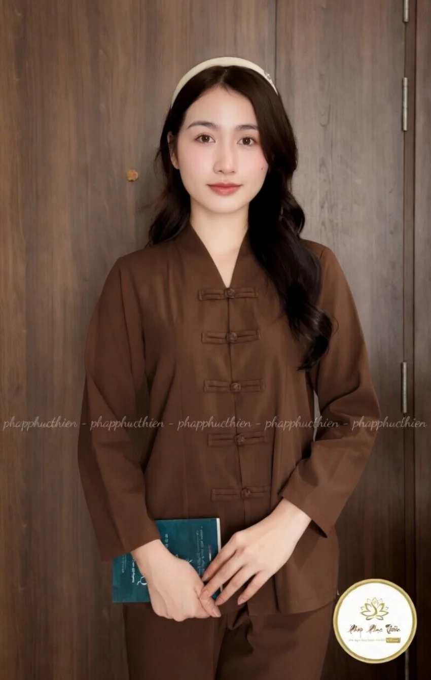 Young woman with long dark hair in a brown traditional Chinese outfit with frog closures, holding a teal book in front of wooden doors.