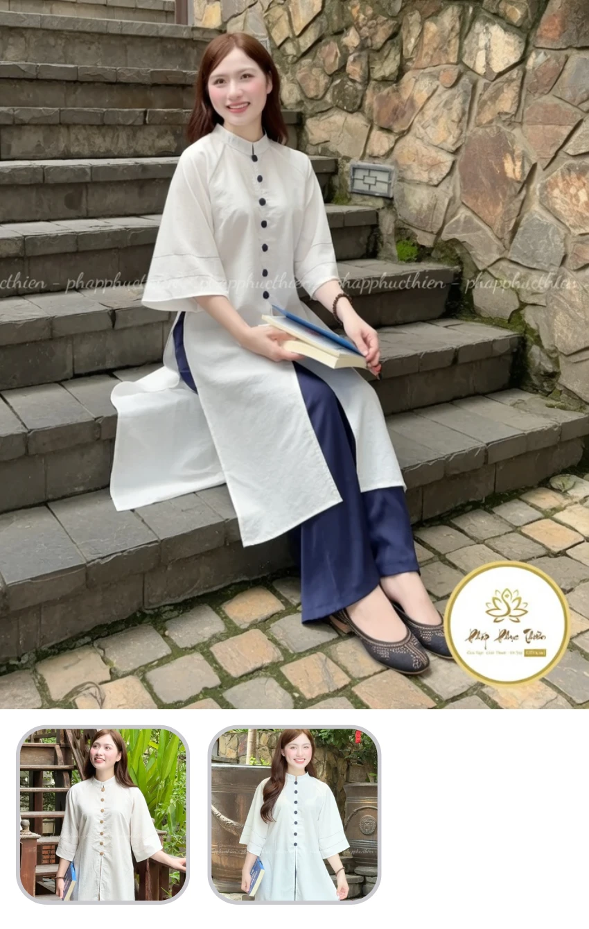 Woman sitting on stone steps in a light white tunic and navy pants, holding two books and smiling at the camera outdoors.