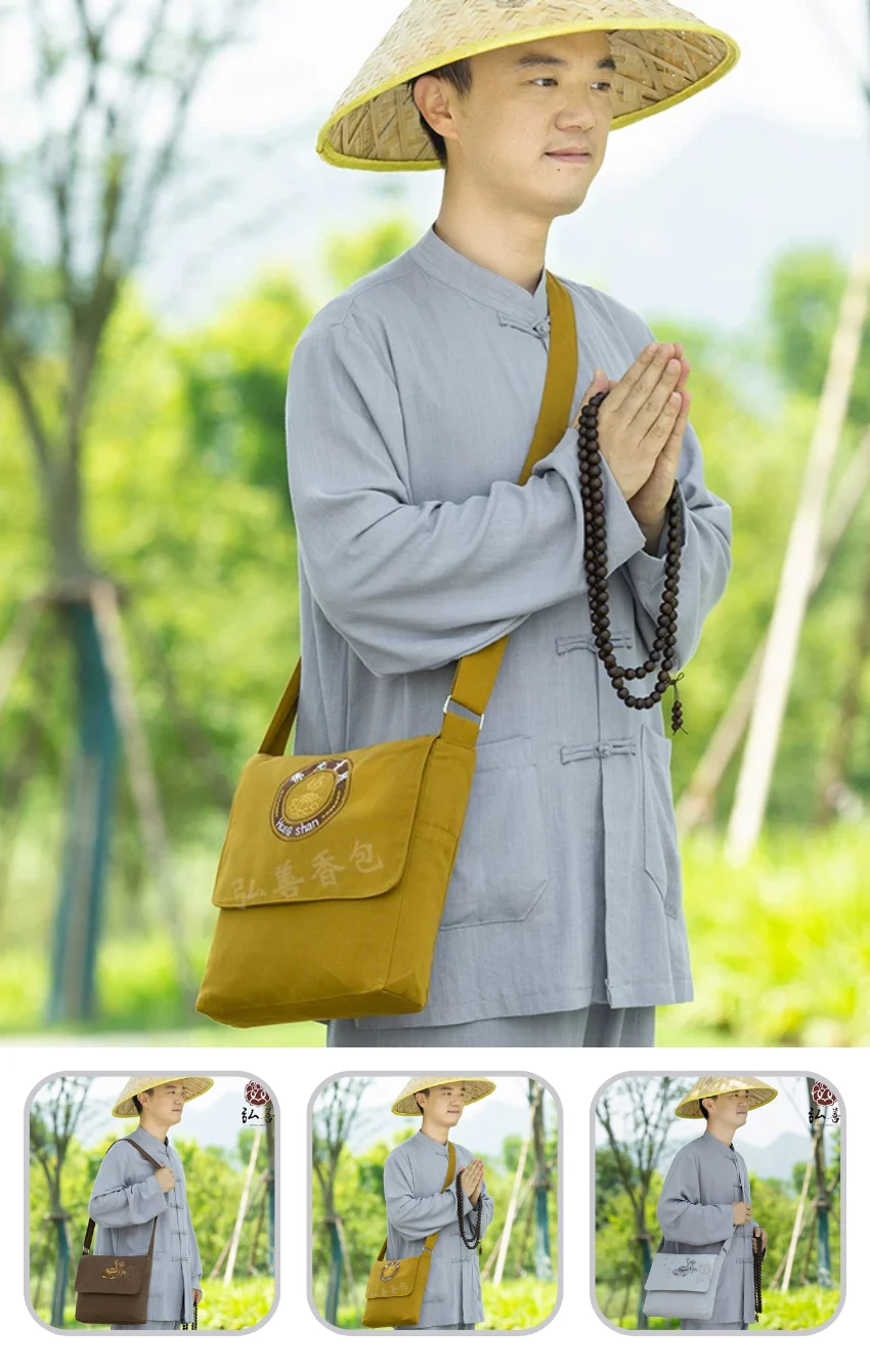 Man in gray monk robes outdoors, wearing a straw hat and holding prayer beads with a yellow shoulder bag.