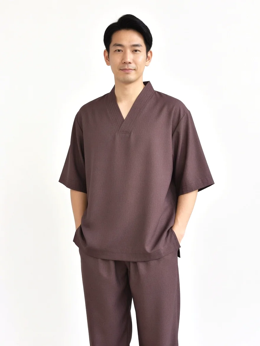 Phap-phuc-v-mau-nau - Pháp Phục Thiền Pháp Phục Man wearing brown samue style outfit with short sleeves hands in pockets standing against a light background