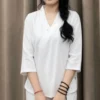 phap-phuc-mau-trang Young woman with long black hair in a side braid, wearing white, holding a woven basket in front of tan curtains.