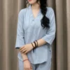 phap-phuc-nu-mau-xanh-ngoc-01 Woman in a light blue traditional-style outfit with a side braid, standing before beige curtains, holding a woven straw bag with a cream bow.