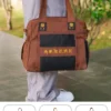 Pháp Phục Brown tote bag with black mesh pocket and yellow embroidery held by a person outdoors