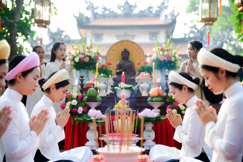 Pháp Phục Women in white robes sit and pray around a Buddhist altar with a statue candles incense and flower offerings outdoors