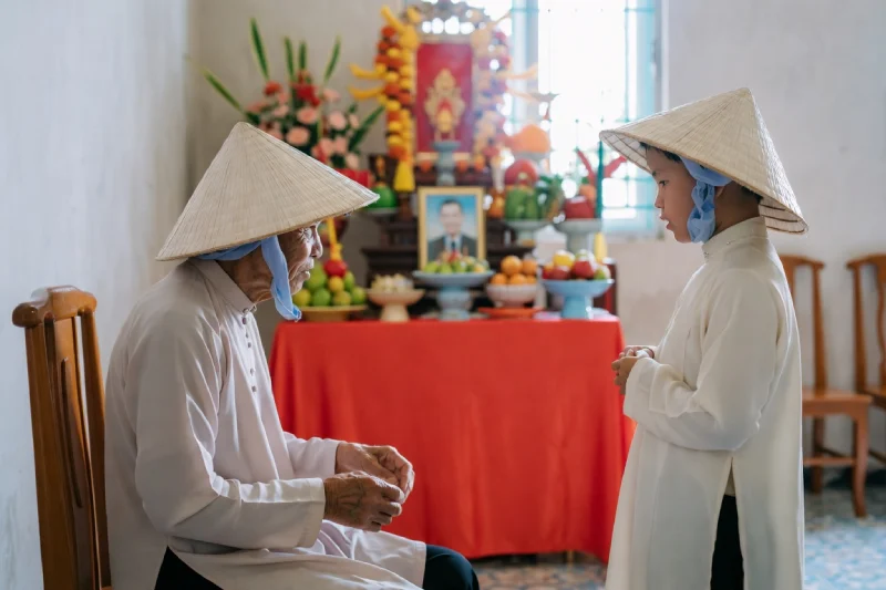 Pháp Phục An elderly woman and a young child in traditional conical hats stand by a temple altar with fruit flowers and a portrait
